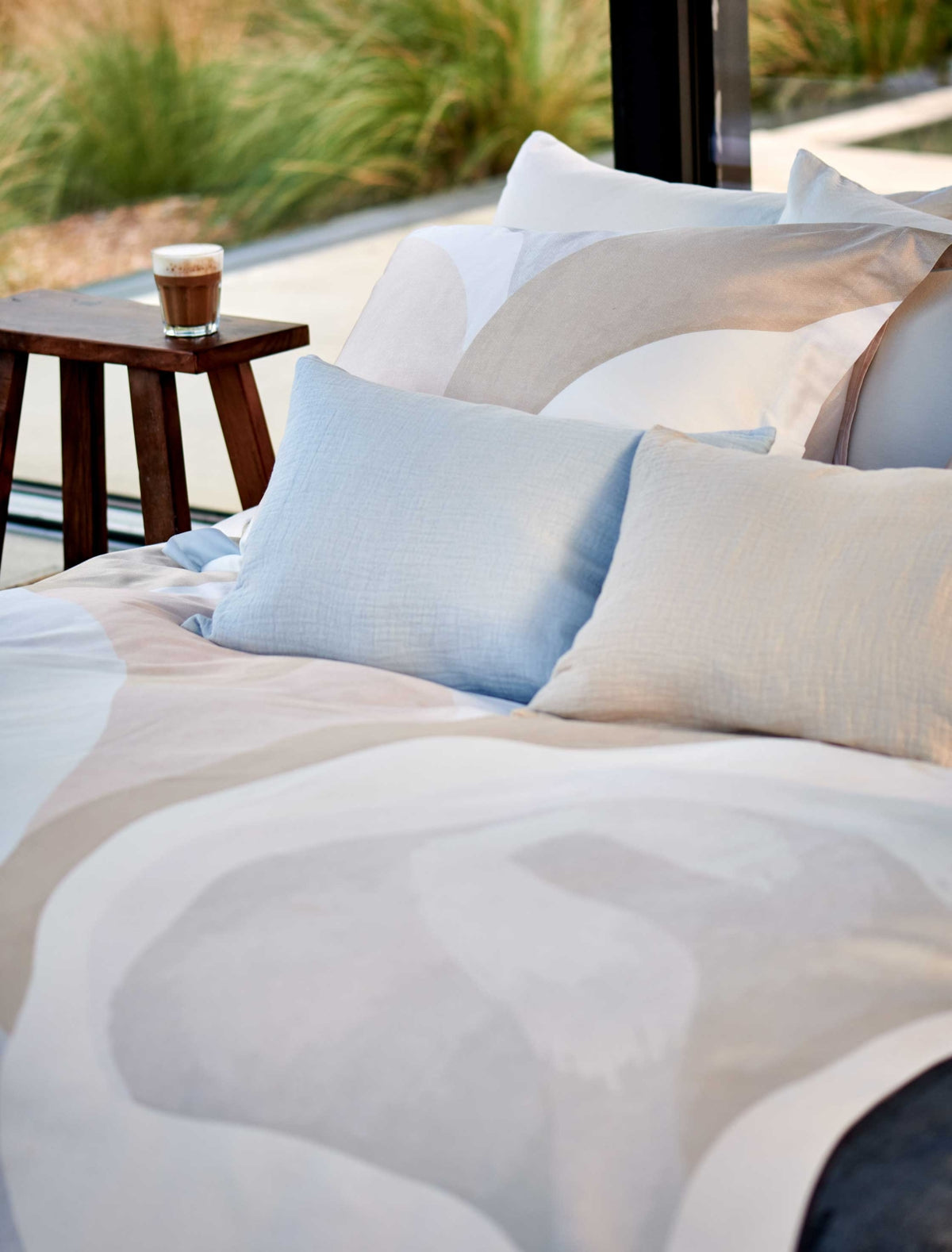 detail shot van een bed met een dekbedovertrek in zachte beige en blauwe kleuren en sierkussens in een beige en lichtblauwe kleur