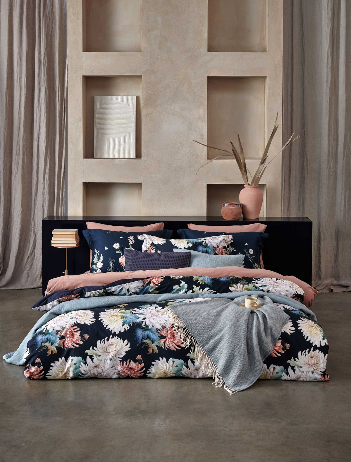 een bed in een rustige, serene omgeving met een bed met een dekbedovertrek in donkerblauw met daarop bloemen geprint, een dekbedovertrek in een roze kleur en een sprei van wol en katoen in een blauwe kleur
