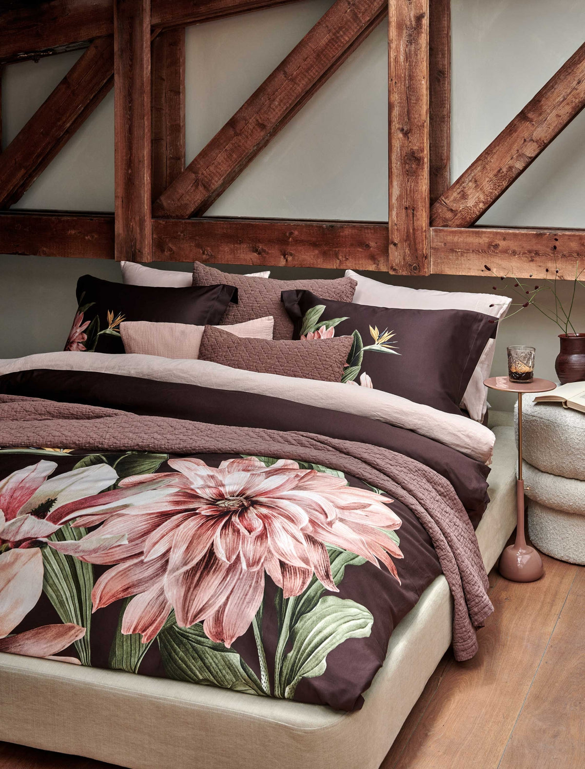 Paradise Bloom dark chocolate dekbedovertrek heeft enorme roze bloemen en mooie bladeren er omheen, op een donkerbruine achtergrond. De bloemen en bladeren hebben nerven, die prachtig geschilderd lijken te zijn. De achterkant van het dekbedovertrek is effen donkerbruin. De kussens hebben een bredere zoom en aan beide zijden in de linkerhoek dezelfde bloemen. 