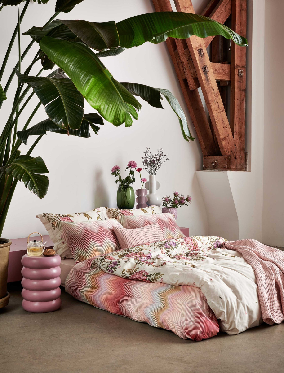 Rose Acacia cream tan dekbedovertrek heeft aan de bovenkant roze en paarse bloemen, die aan takken hangen met kleine dwarrelende blaadjes. De achterkant van het dekbedovertrek is effen beige. Het design oogt rustig en zacht.